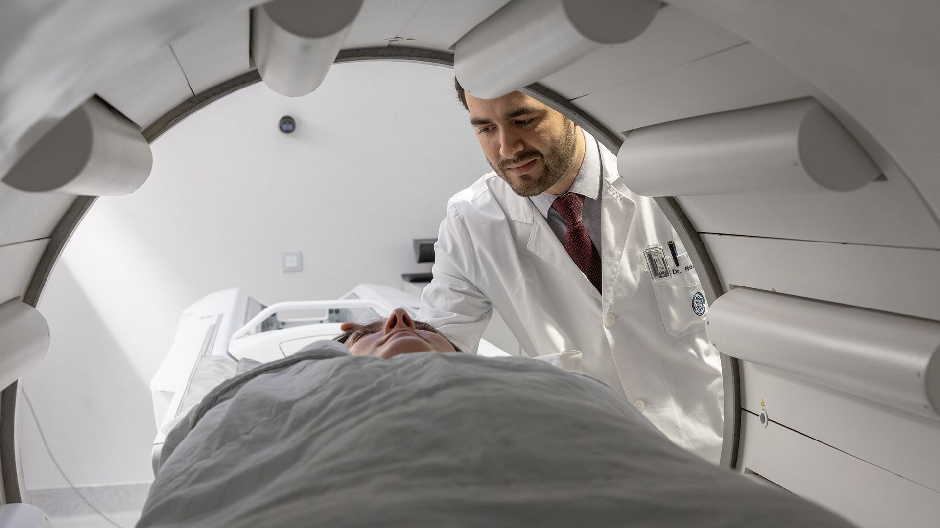A nuclear medicine physician in a white coat examining a patient inside a PET/CT scanner ring