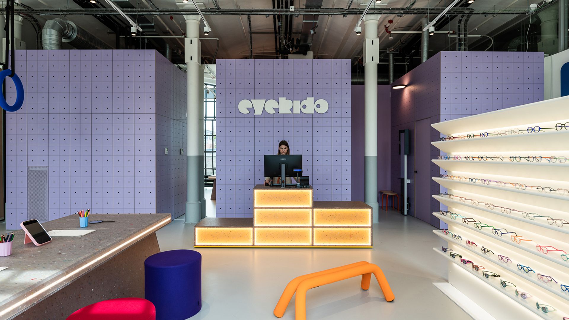 Interior of the Eyekido children's eye care centre with purple pegboard walls, a reception desk and illuminated eyewear display shelves