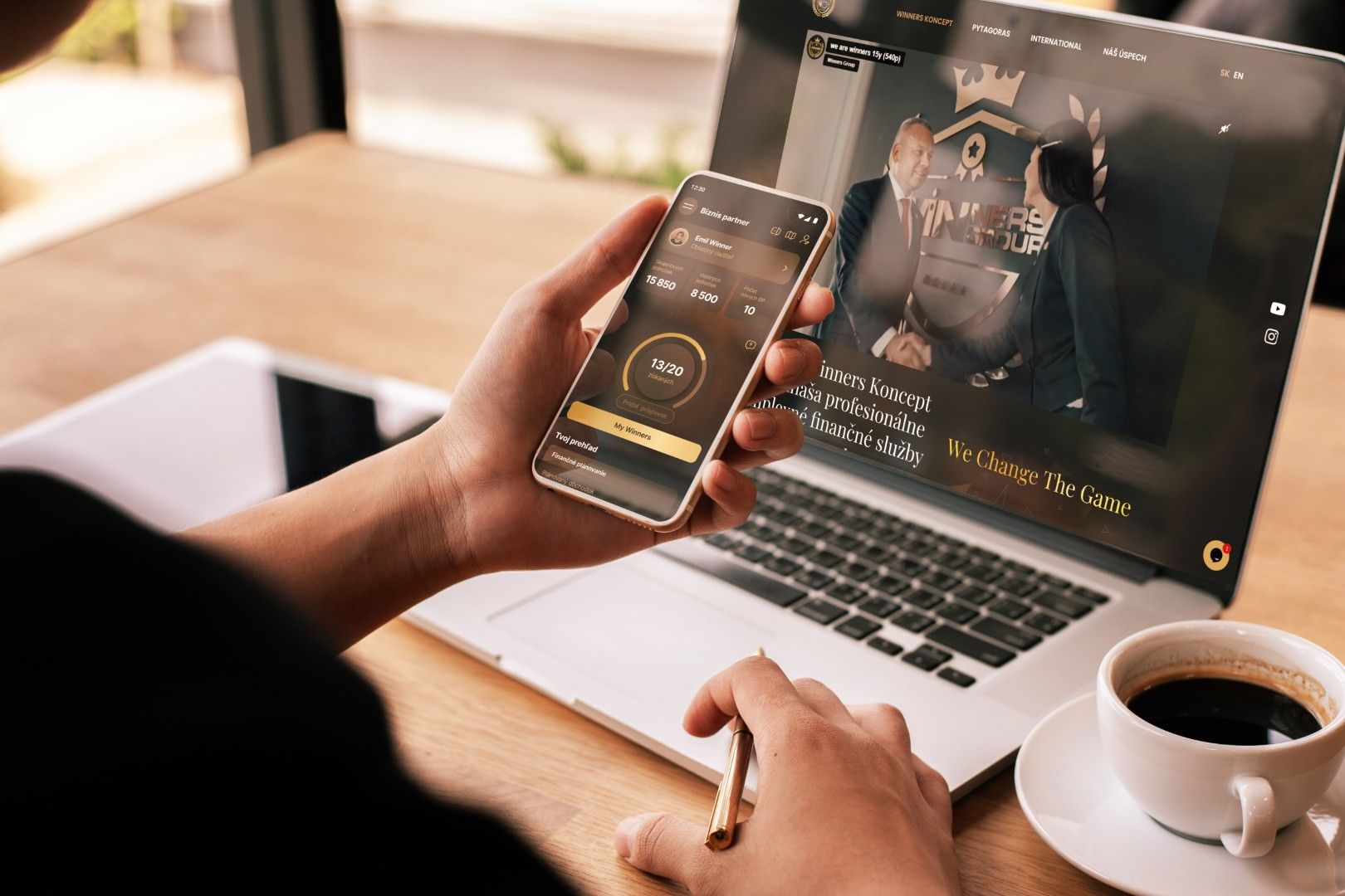 Broker app on phone alongside laptop showing Winners Group website at a cafe